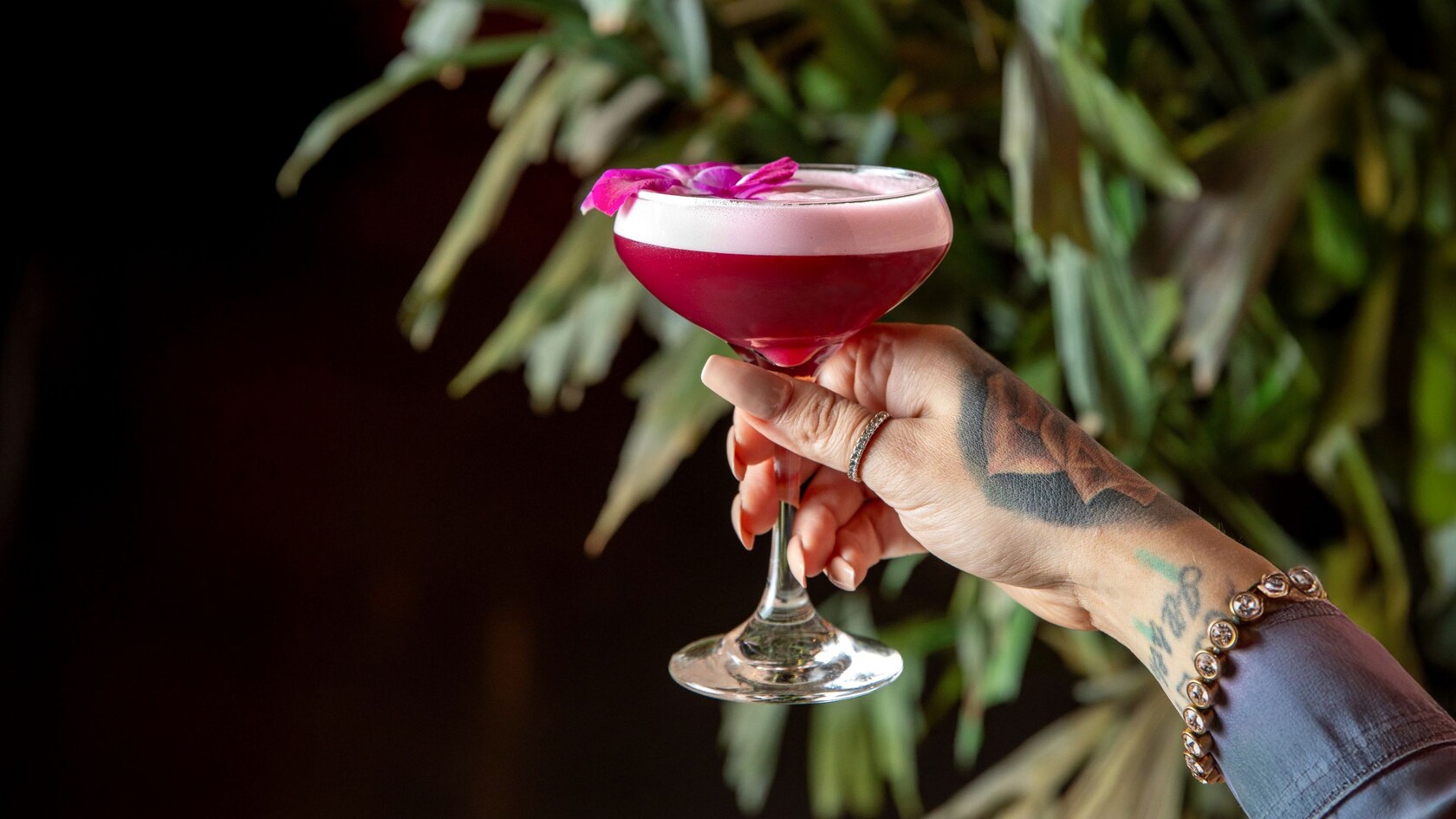 A hand holding a cocktail garnished with a hibiscus flower