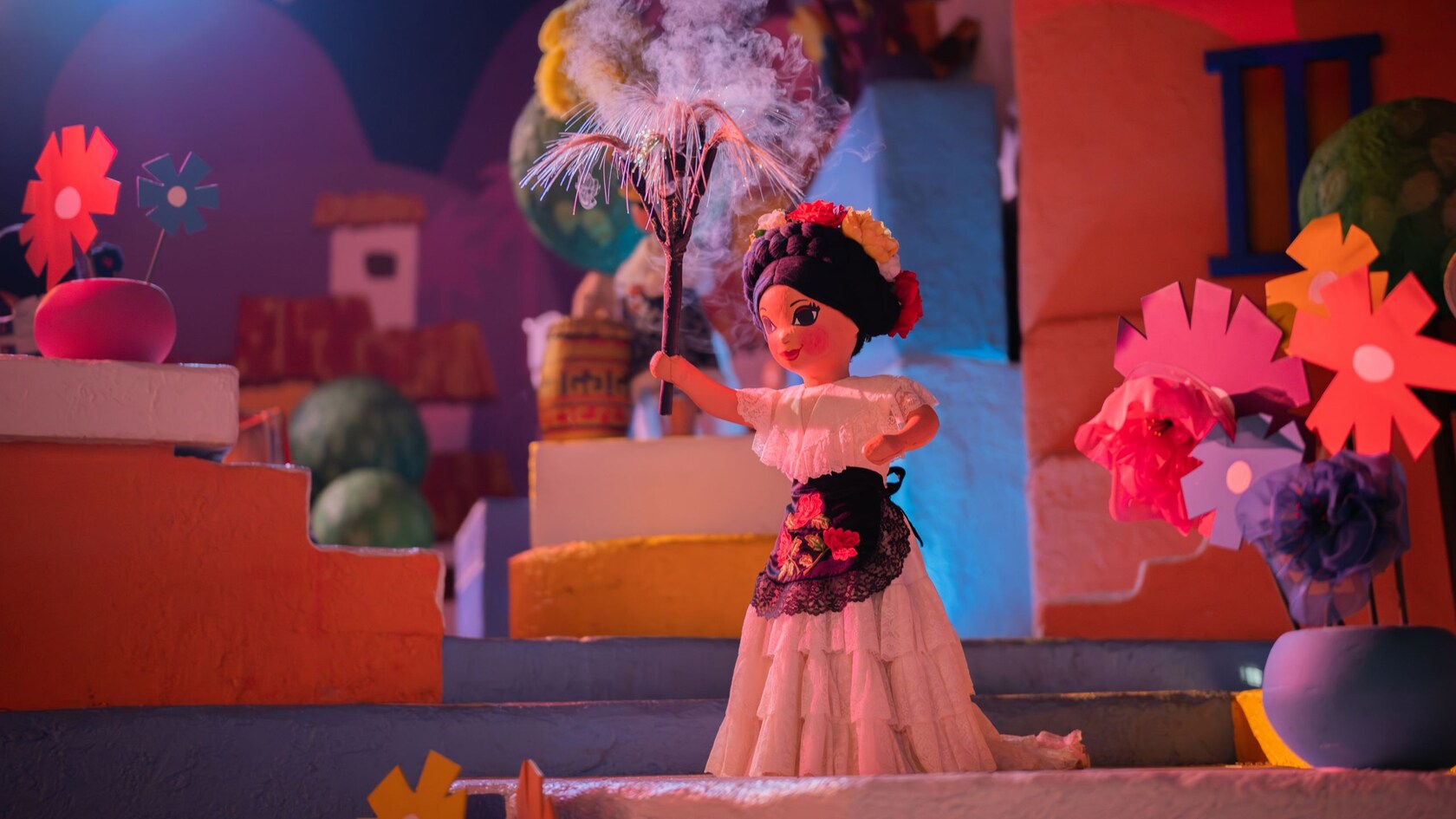 A Mexican girl doll with vases of paper cutout flowers around her at Gran Fiesta Tour Starring The Three Caballeros