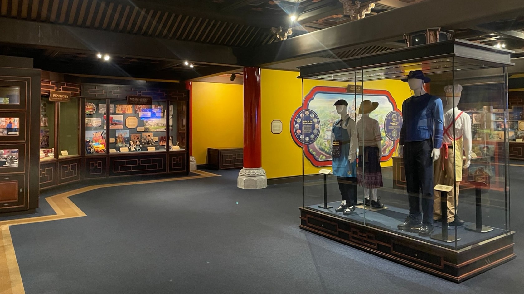 The interior of House of Whispering Willows at Shanghai Disney Resort featuring display cases with Disney artwork and 4 mannequins in vintage costumes