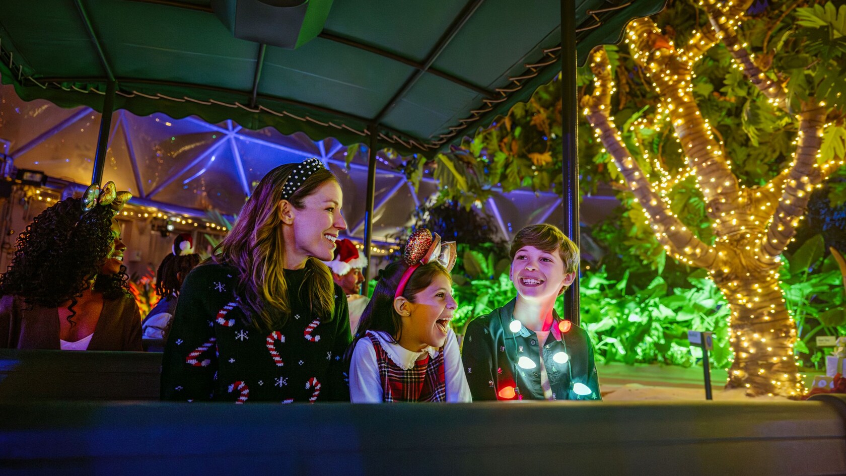 A family in holiday attire viewing the Glimmering    Greenhouses lighting effects from a tandem boat  