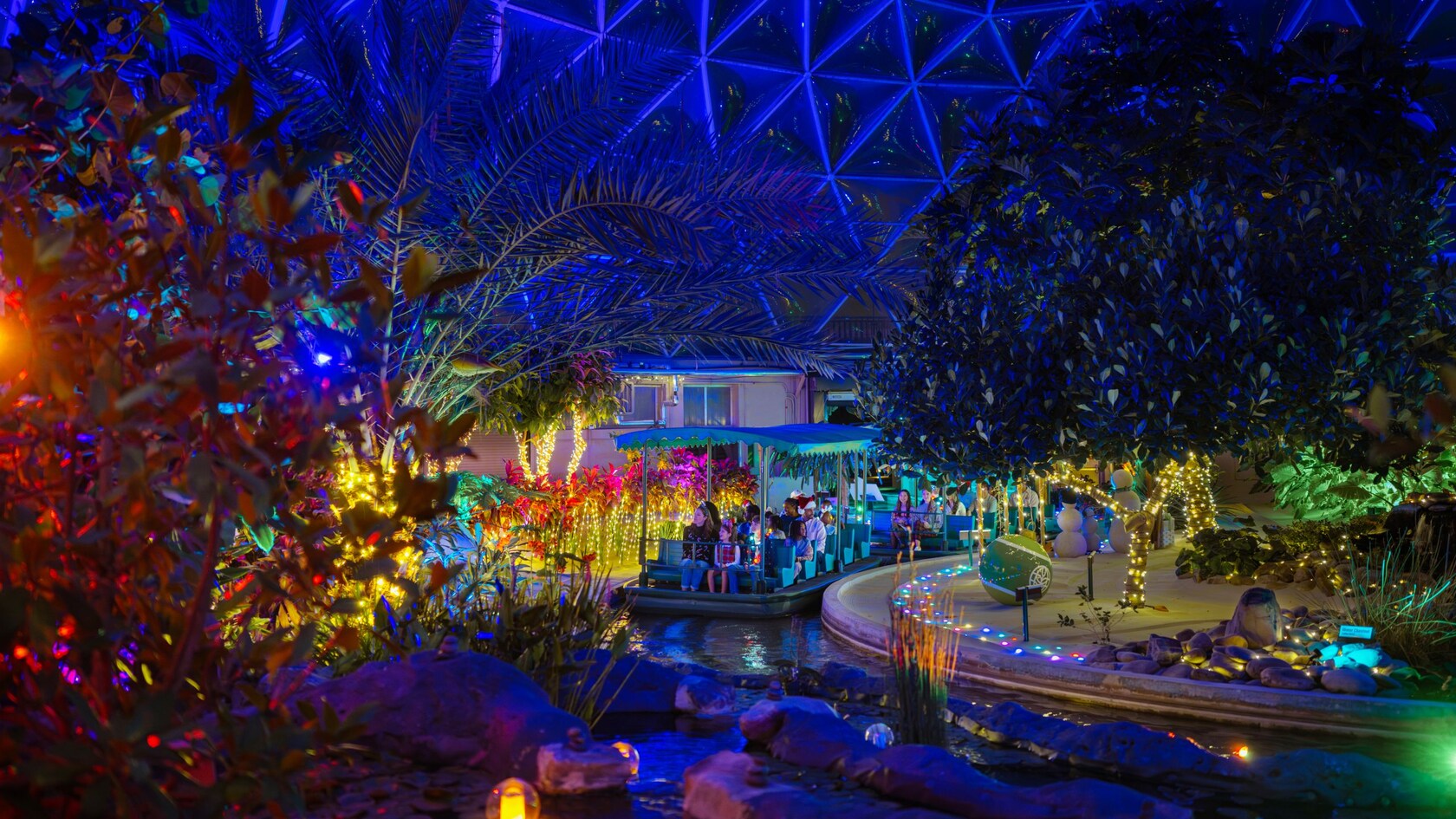 Guests riding in tandem boats past decorated trees in    Glimmering Greenhouses at Epcot 