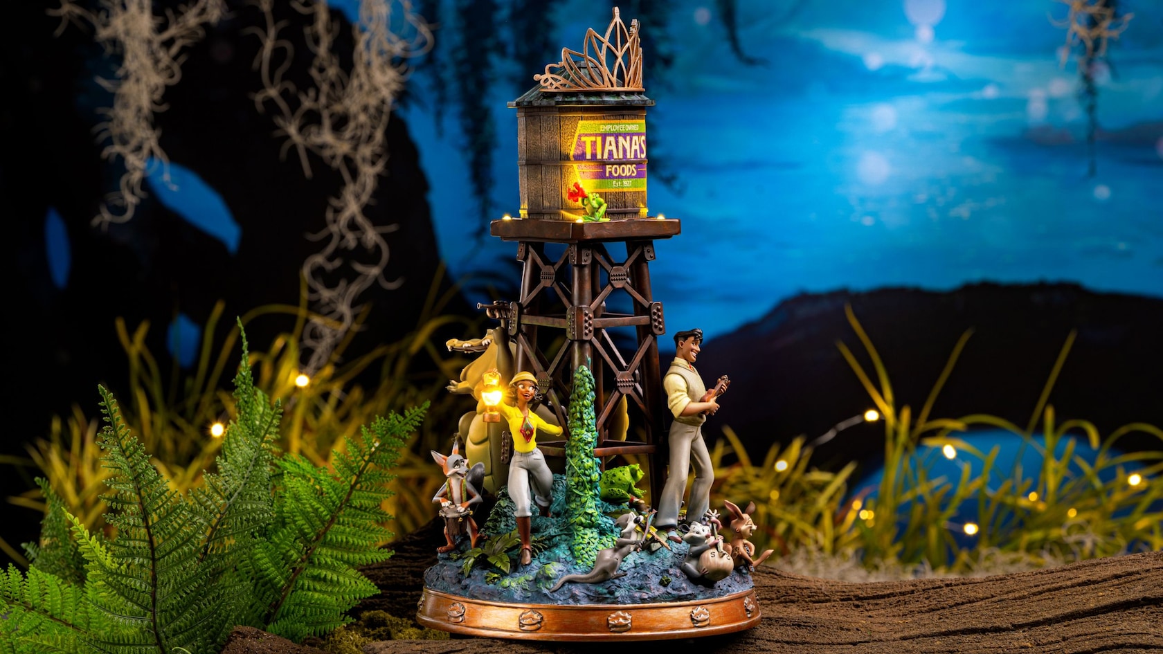 A toy figurine with Princess Tiana and Prince Naveen in adventure attire along with the critters from Tiana’s Bayou Adventure under a tower and the words ’Tiana’s Foods’