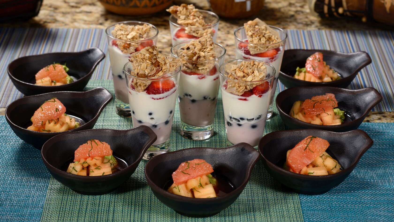 Several bowls of fruit and several glasses filled with a fruit and yogurt parfait