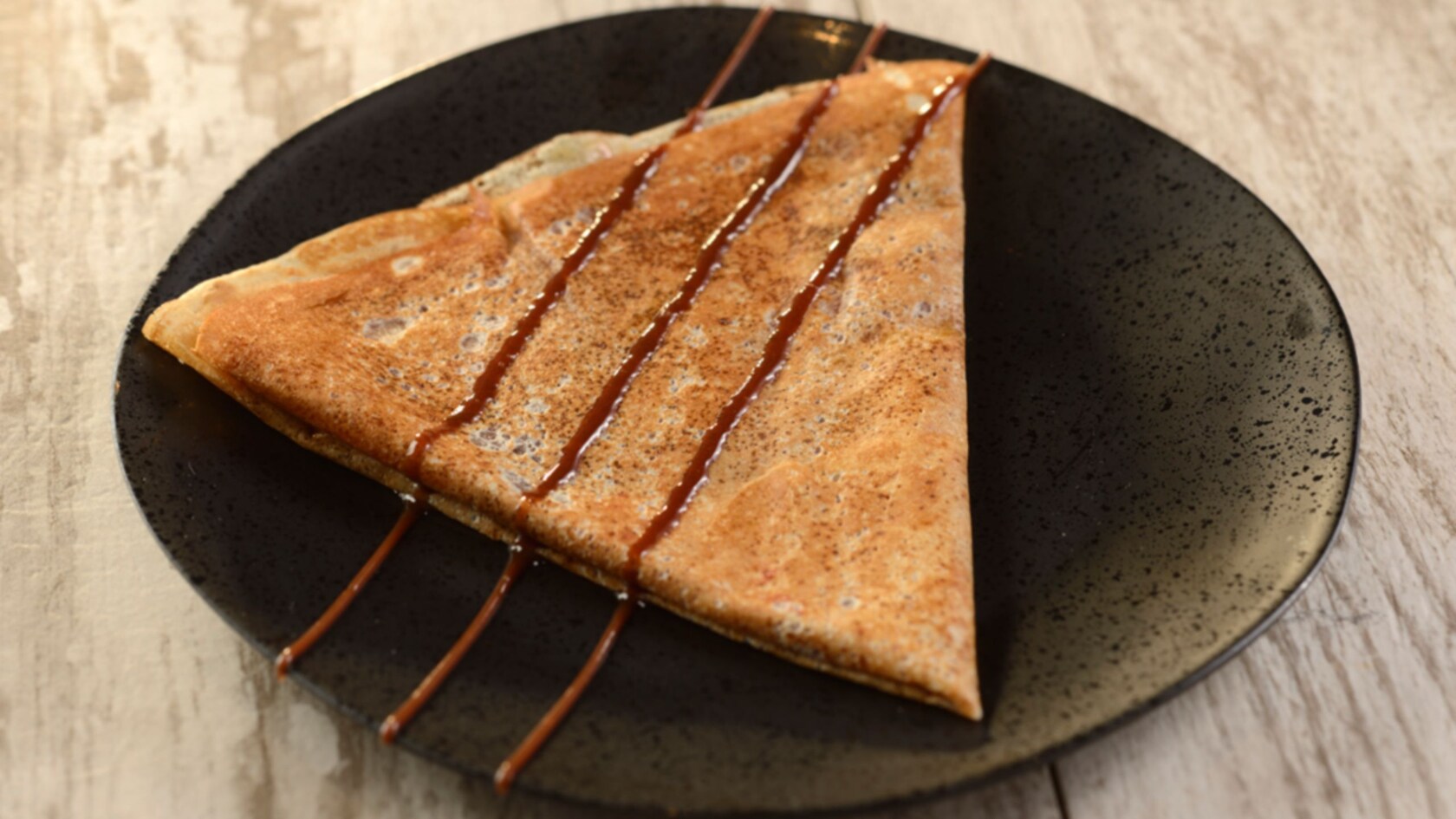 A noisette crepe with chocolate drizzled on top served on a plate