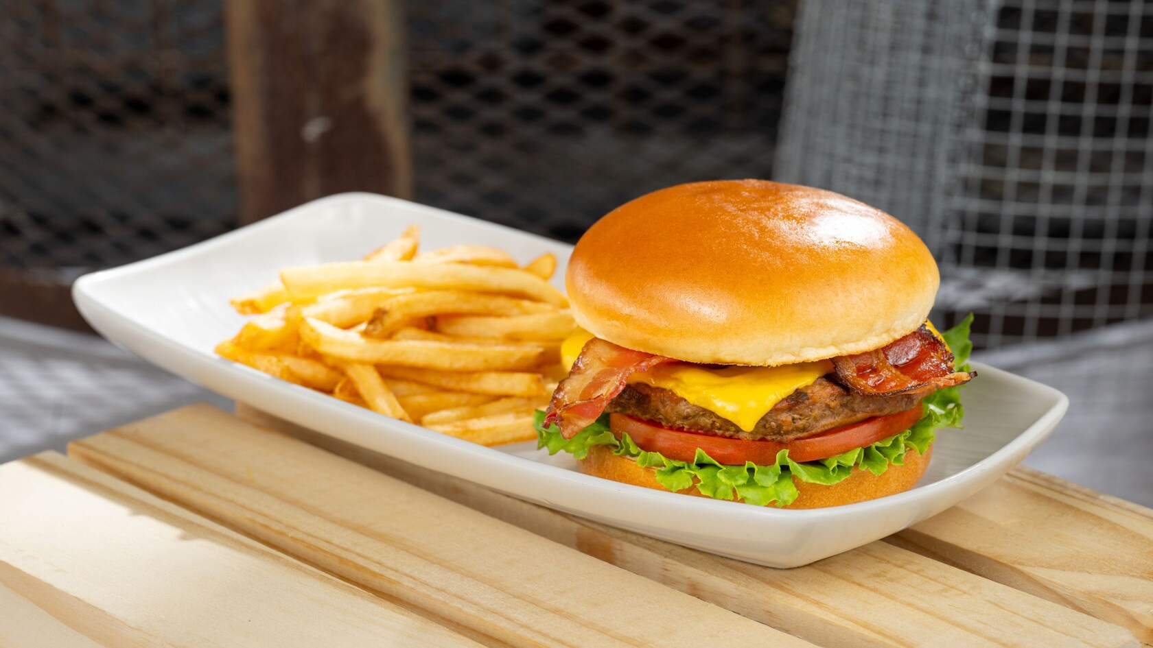 A bacon cheeseburger atop a tomato slice and lettuce, with a side of fries