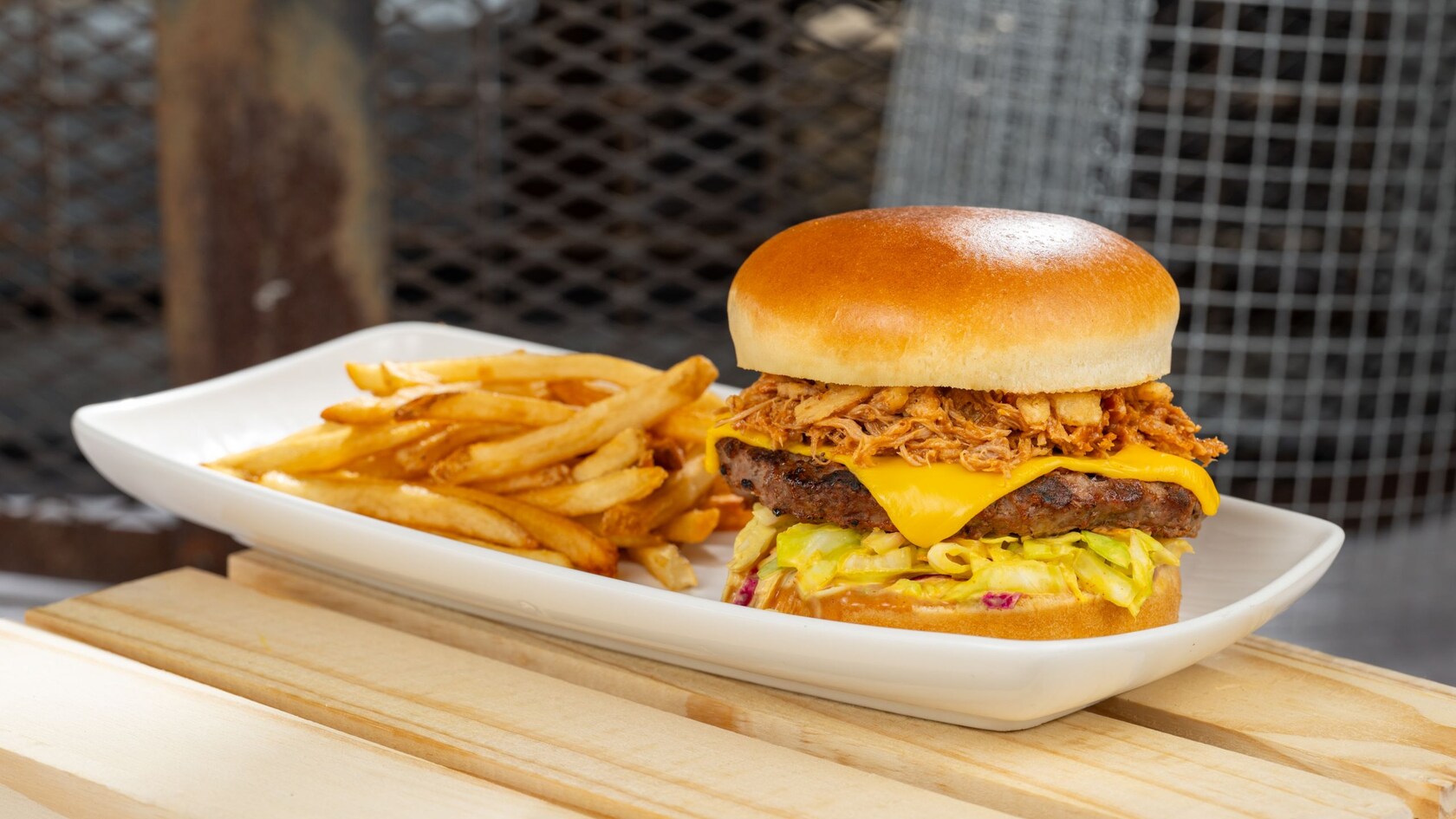 A beef burger topped with pulled pork, cheese, coleslaw and barbecue sauce, with a side of fries