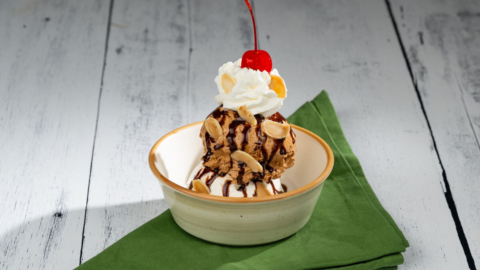 An ice cream sundae topped with whipped cream, chocolate sauce, a cherry and nuts