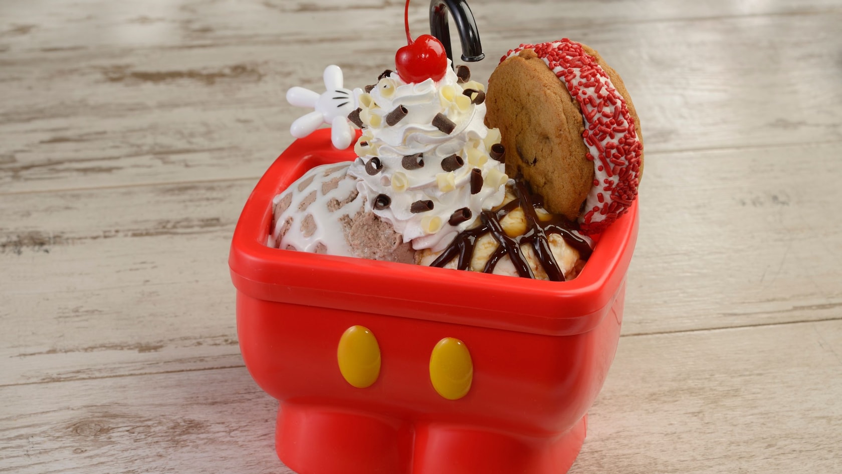 An ice cream sundae complete with whipped cream and a cookie sandwich served in a bowl shaped like Mickey Mouse’s pants