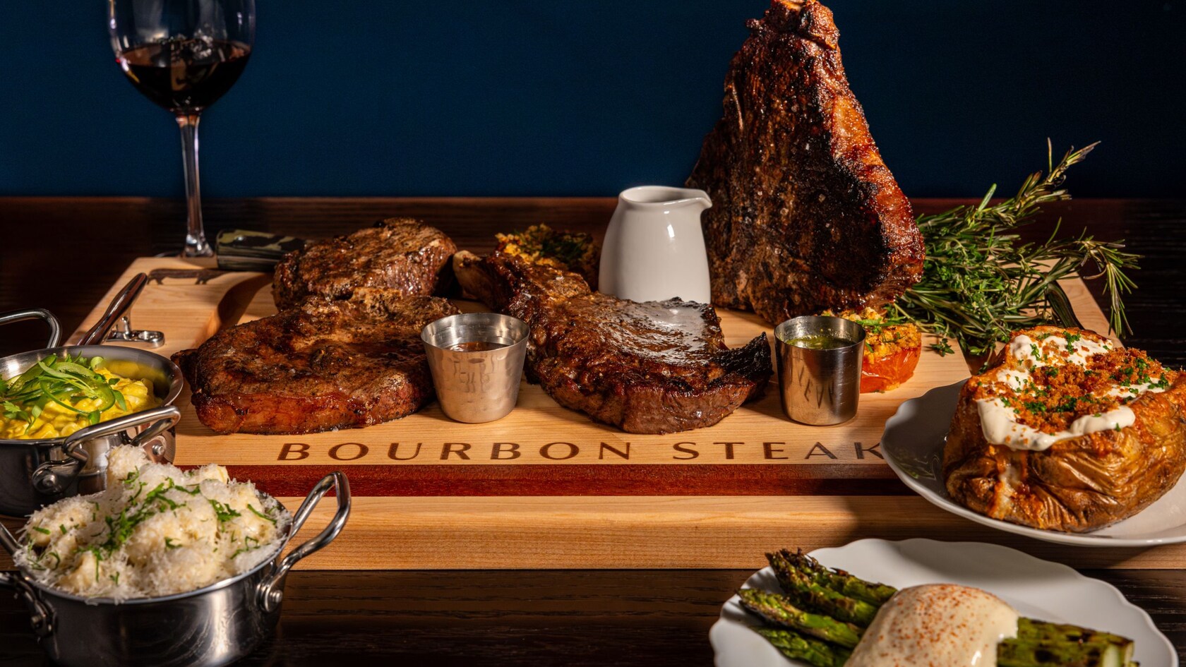 A platter of steaks with plates of asparagus, loaded potato, jalapeno creamed corn and creamy mac and cheese