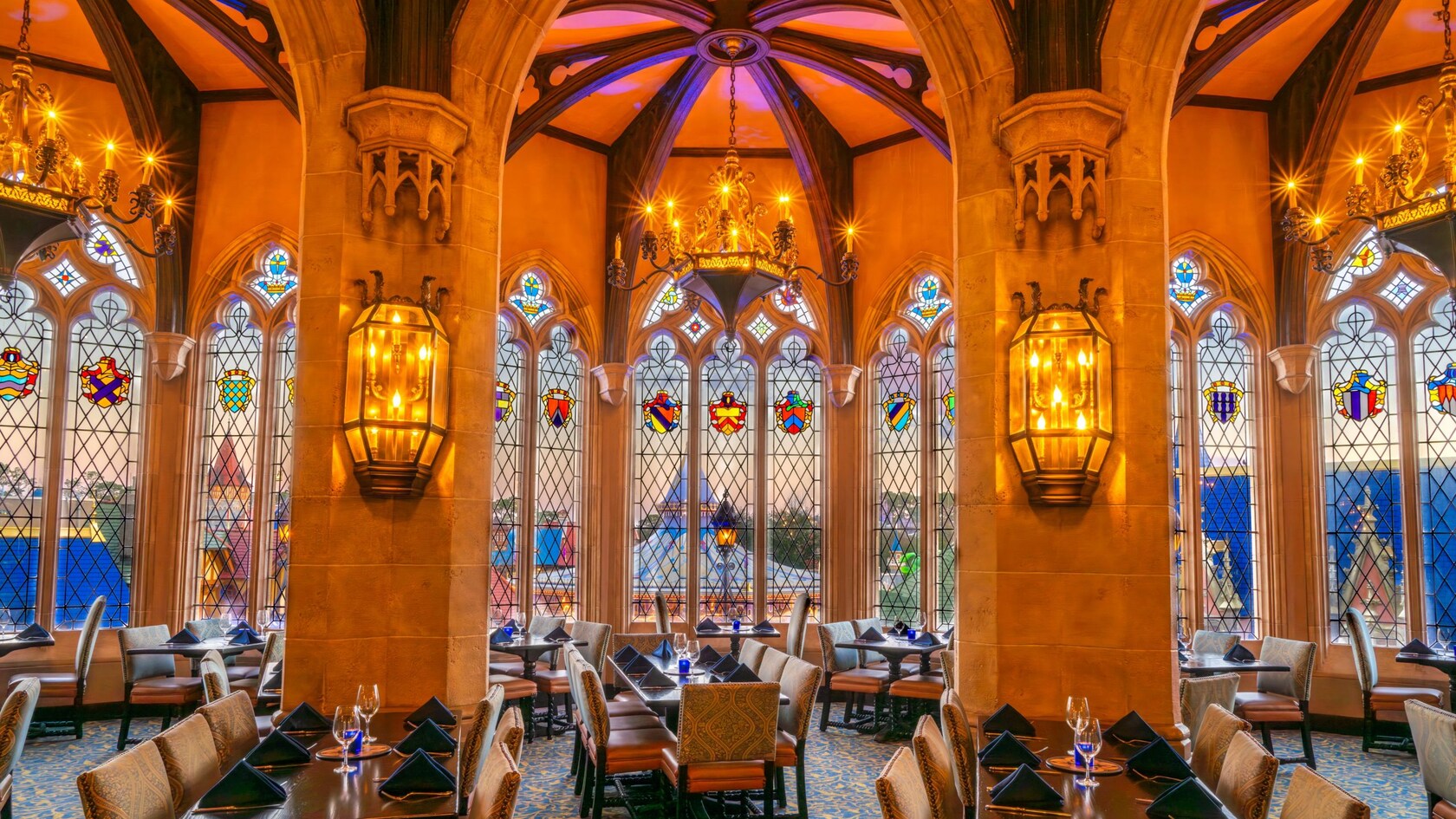 A grand dining room with high arched ceilings, stained glass windows, chandeliers and tables set for Guests