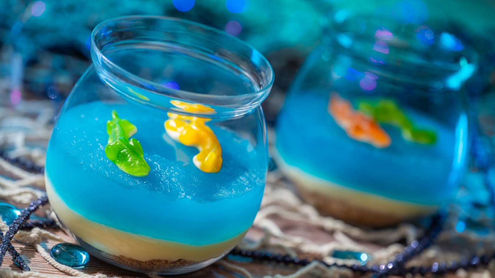Two fishbowl shaped dessert cups filled with a custard base topped with gelatin and gummy fish  