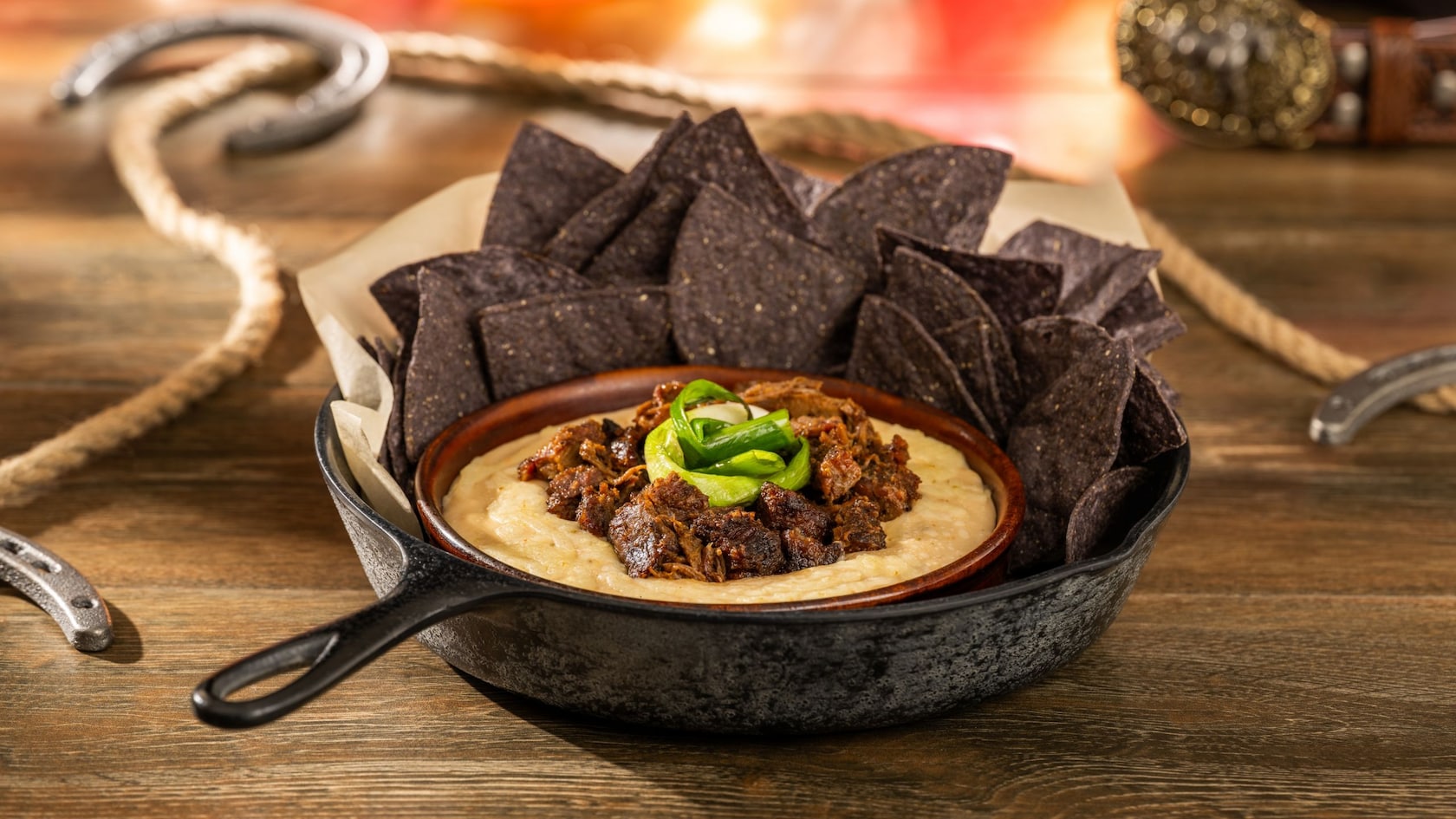 A queso fundido served in a pan, featuring barbecue burnt ends and tortilla chips