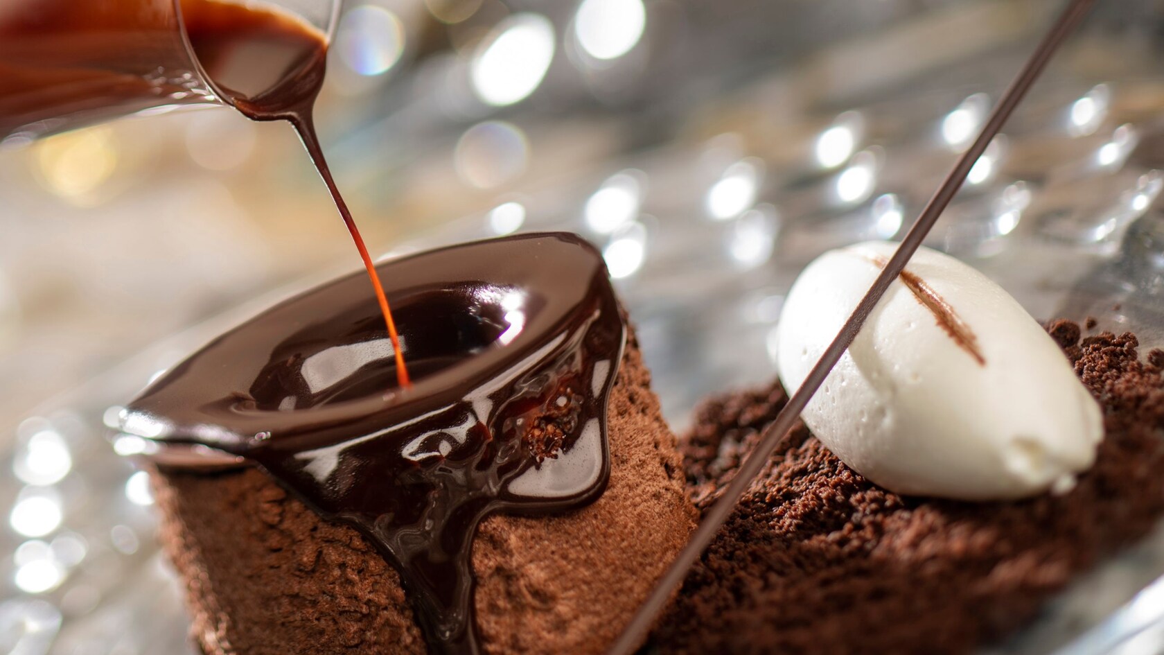 Chocolate sauce being poured over a chocolate cake on a glass plate