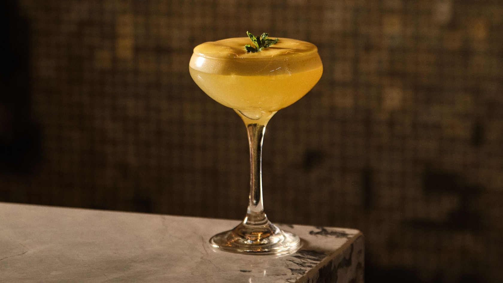 A cocktail in a stemmed glass garnished with an herb sprig