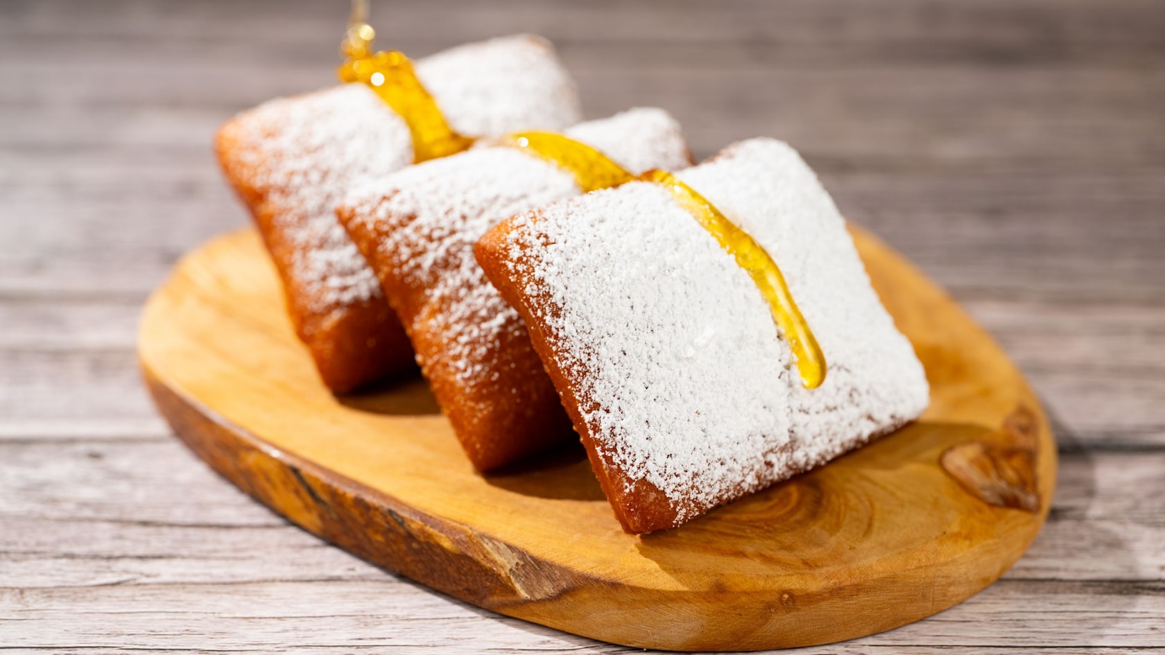 Beignets cubiertos de azúcar glas y rociados con miel sobre una tabla de madera