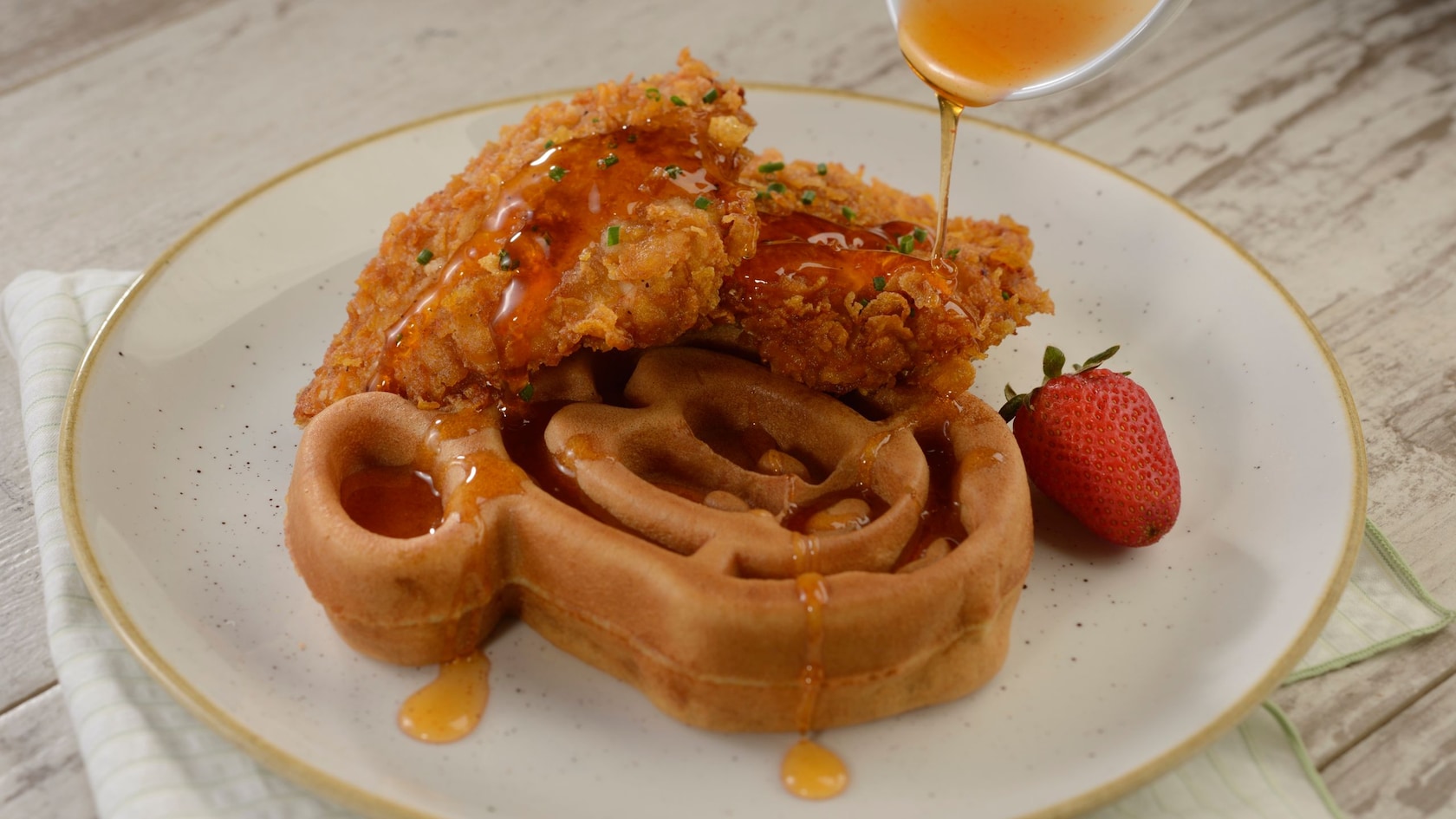 A waffle in the shape of Mickey’s head and 2 pieces of fried chicken breast, with Sriracha Honey drizzle