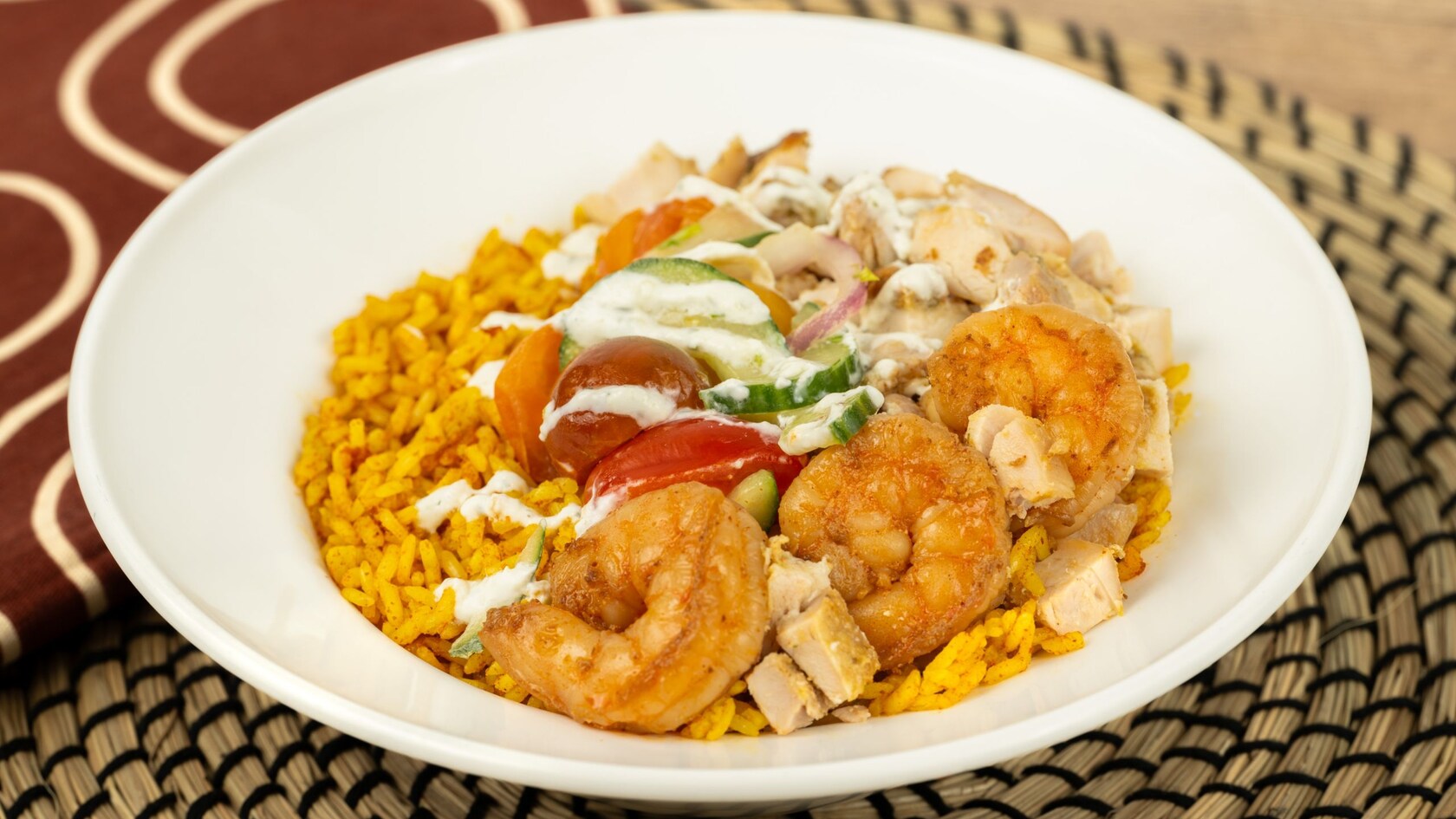 A Shrimp Rice Bowl with peri peri-marinated shrimp on jollof rice with kachumbari tomato salad and tzatziki sauce	