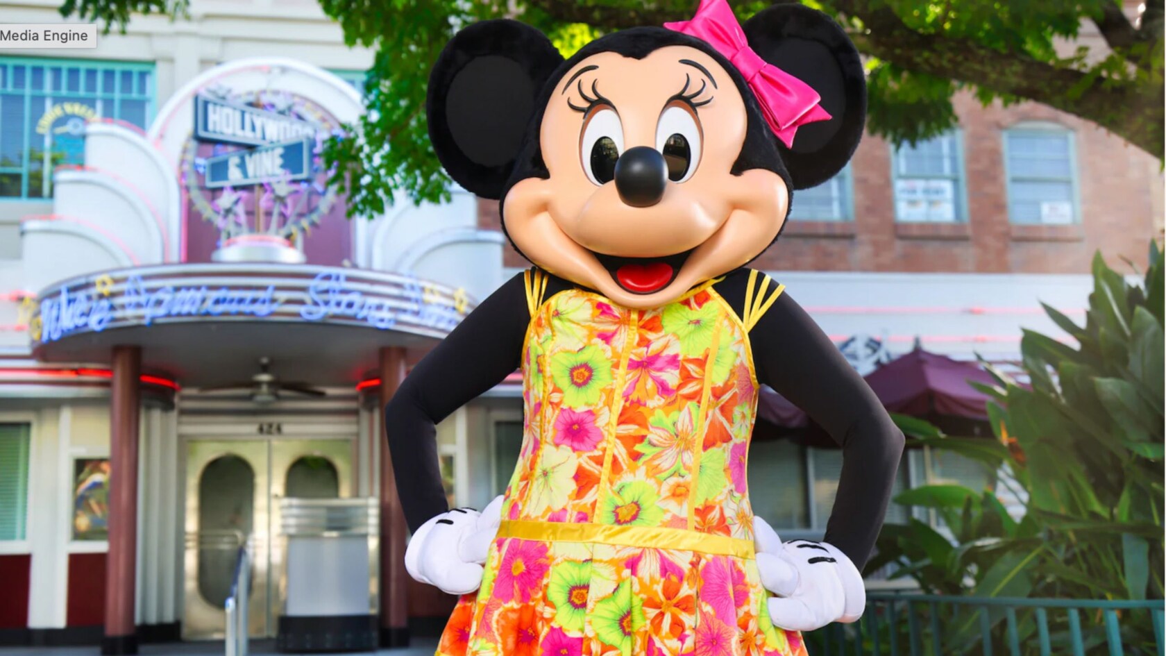 Minnie Mouse wearing a floral dress and a bow in front of Hollywood & Vine restaurant