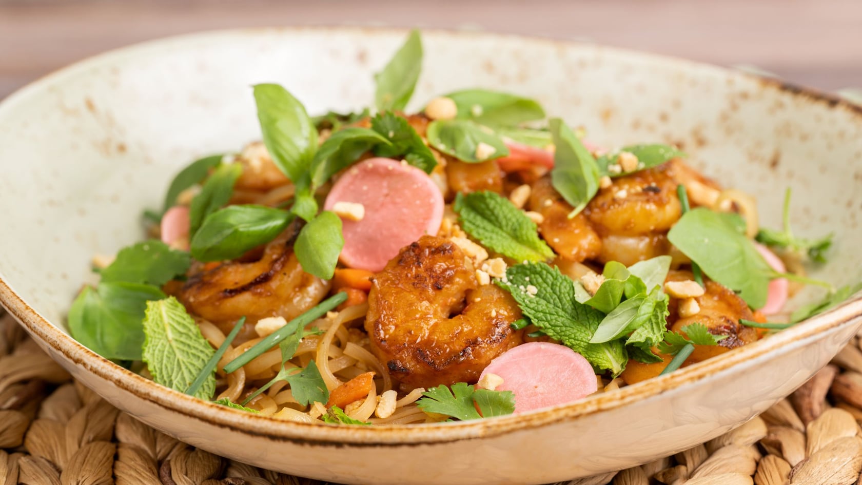 A bowl of rice noodles with sauteed shrimp, pickled radish, eggs, toasted peanuts and herbs