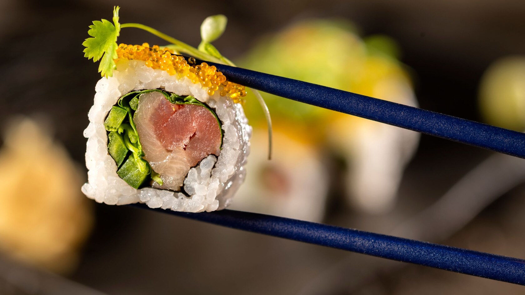 A piece of sushi held between a pair of chopsticks