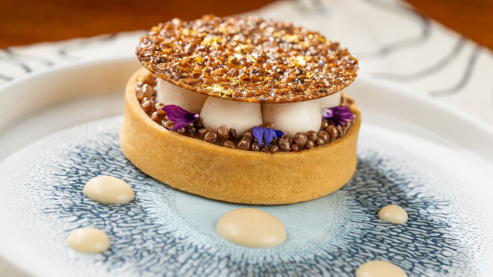 A tart topped with brown butter panna cotta spheres, surrounded by cocoa nib tuille, edible flower petals and maple creme anglaise