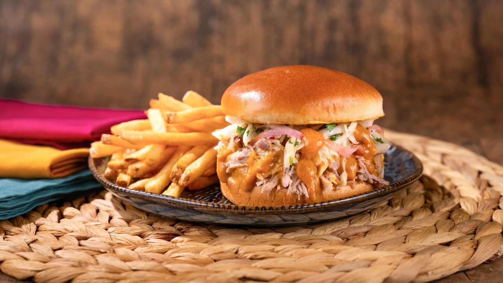 A Smoked Pork Sandwich topped with coleslaw and sauce served with French fries on a plate