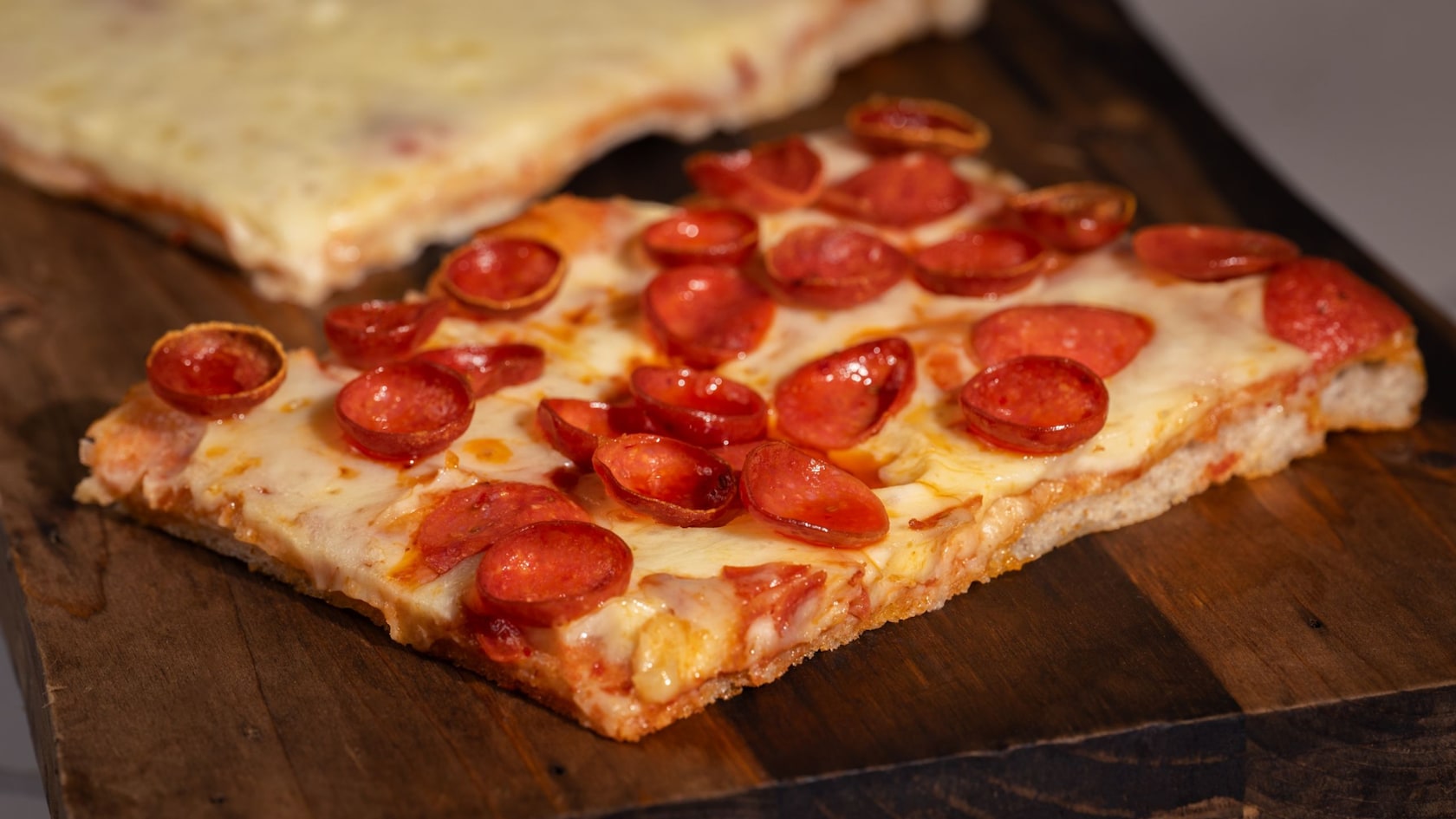 Two slices of Sicilian style pizza, one with just cheese and the other with pepperoni topping