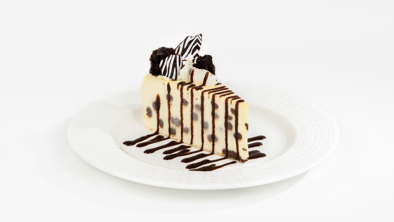 Slice of Marbled Swirled Cheesecake drizzled with chocolate sauce and topped with whipped cream and mini brownies