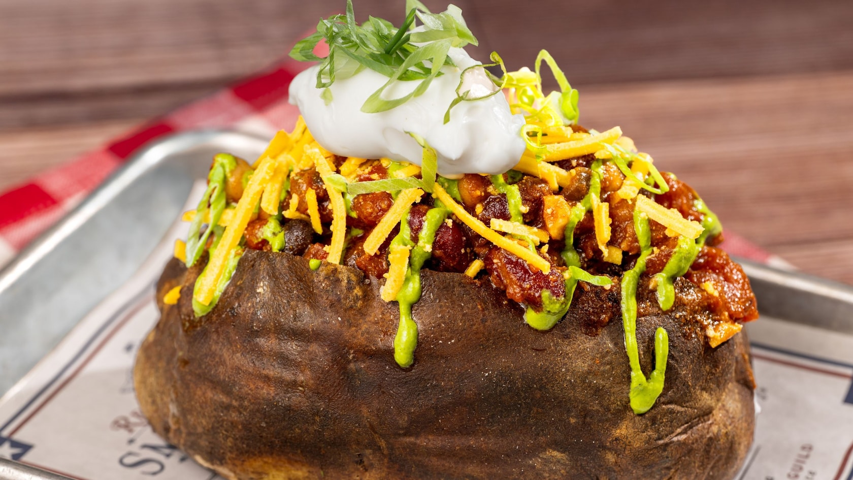 A loaded baked potato topped with chili, cheese, sour cream and avocado sauce