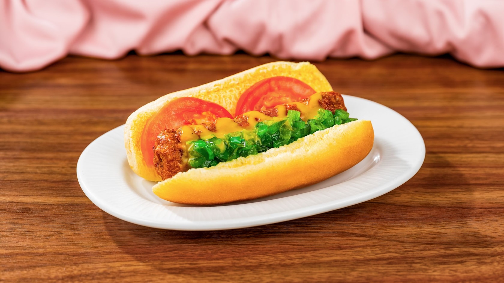 A plant based food item in the shape of a hotdog, with tomatoes, mustard, aioli and green relish on a bun
