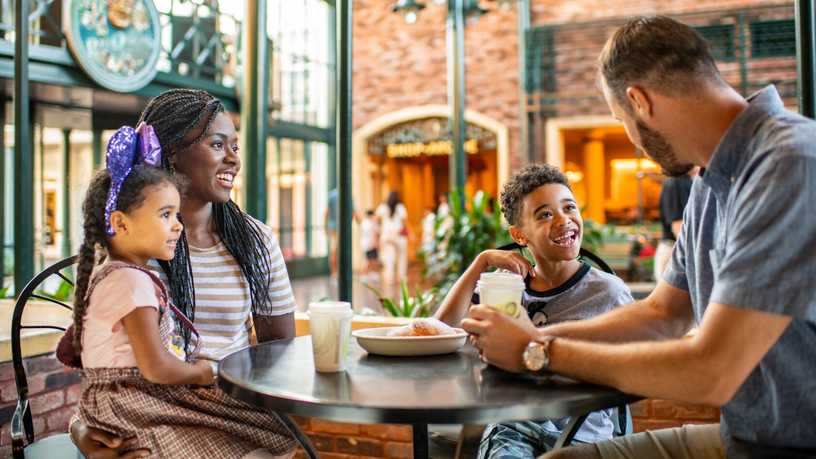 Uma família de 4 pessoas sentada à mesa apreciando bebidas quentes e beignets.