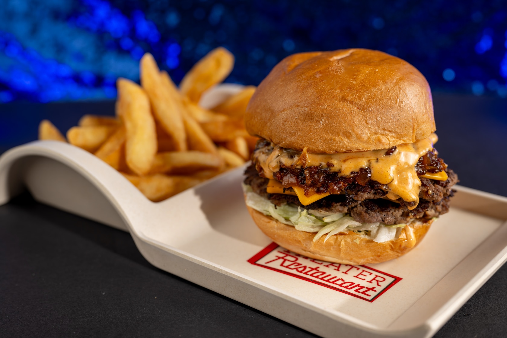 Una hamburguesa especial con dos hamburguesas aplastadas, queso americano, trozos de lechuga, mermelada de tocino y salsa con un acompañante de papas fritas