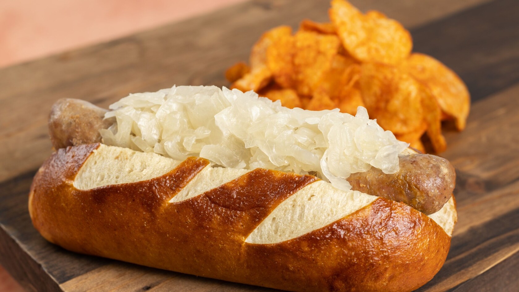 A bratwurst in a pretzel bun, topped with sauerkraut and served with potato chips