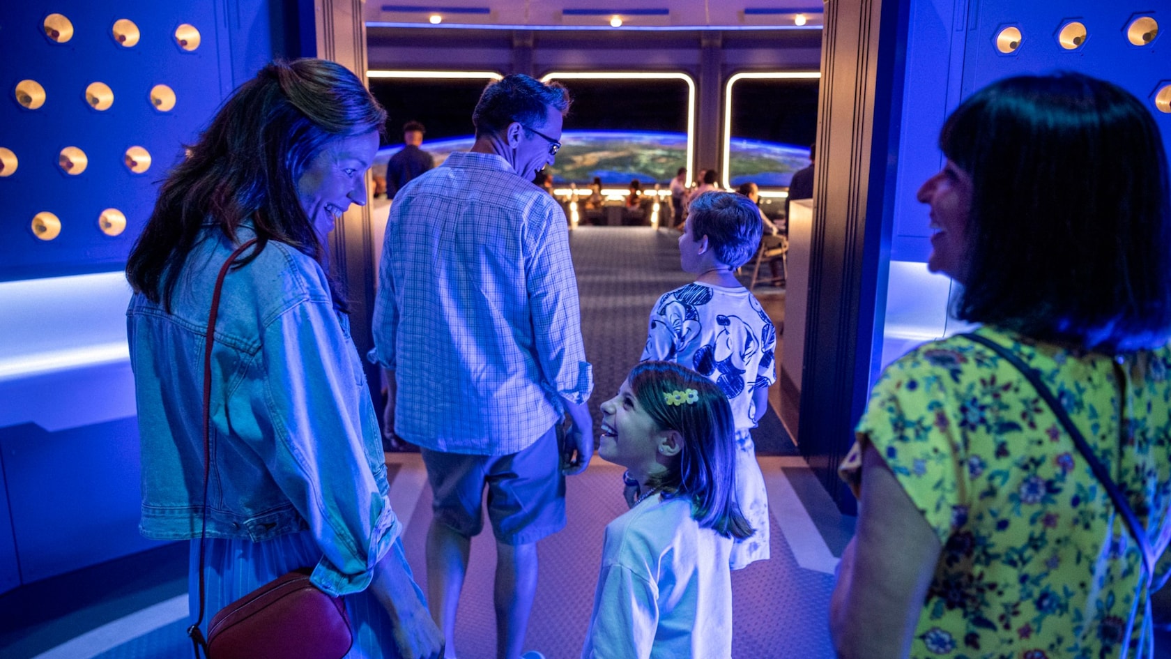 Una familia baja de un ascensor futurista a un comedor con vistas a la Tierra desde el espacio
