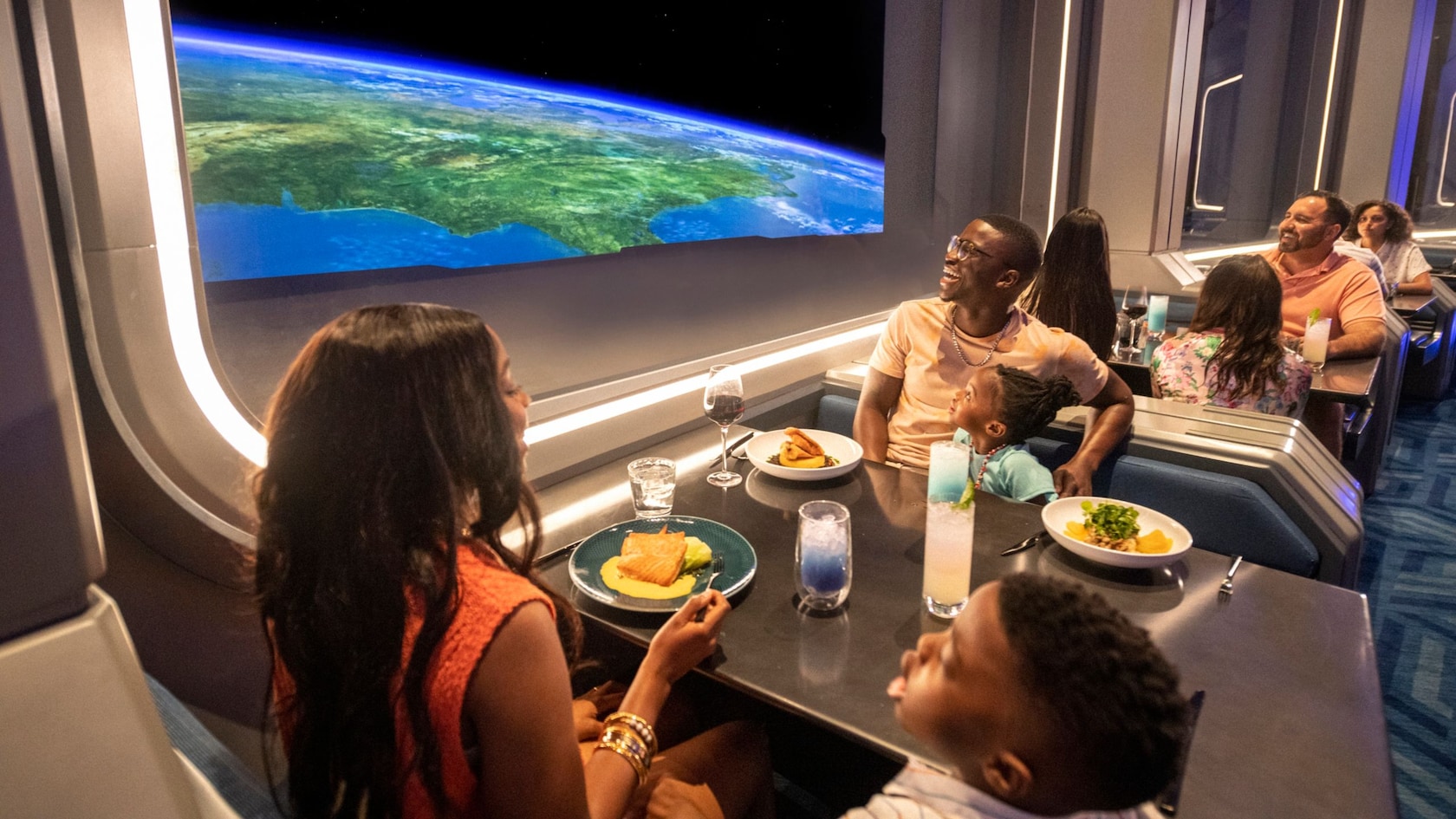 Las familias se sientan en las cabinas del restaurante y disfrutan de la comida, las bebidas y una vista de la Tierra desde el espacio