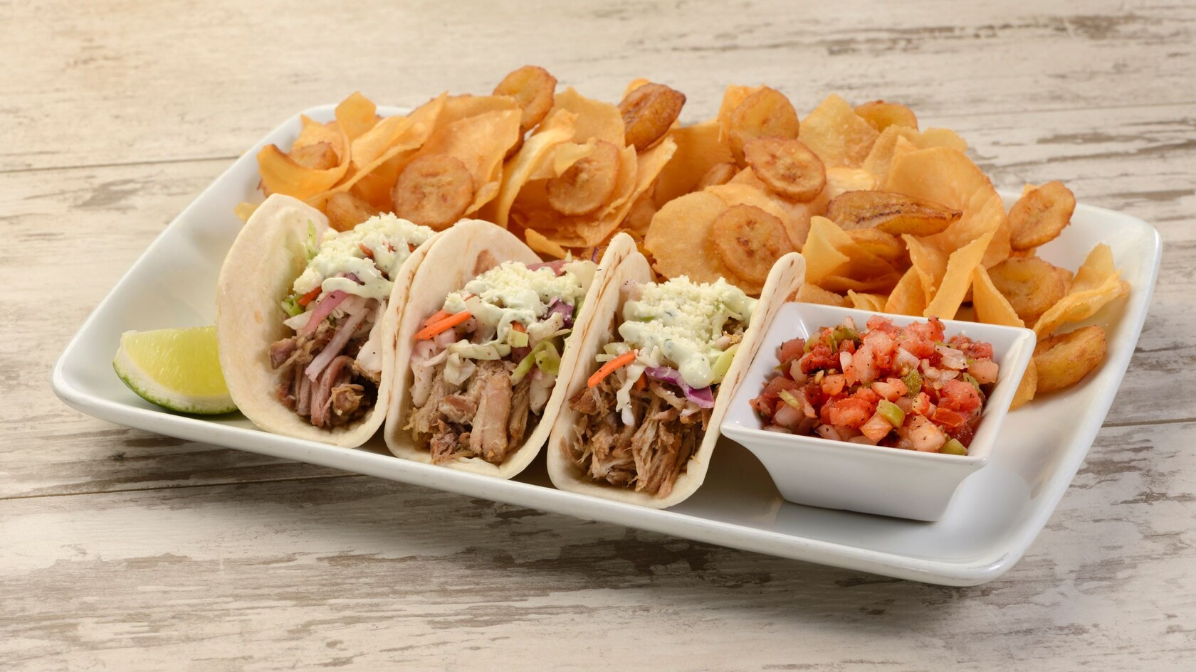 Three tacos served on a plate with salsa and yuca chips