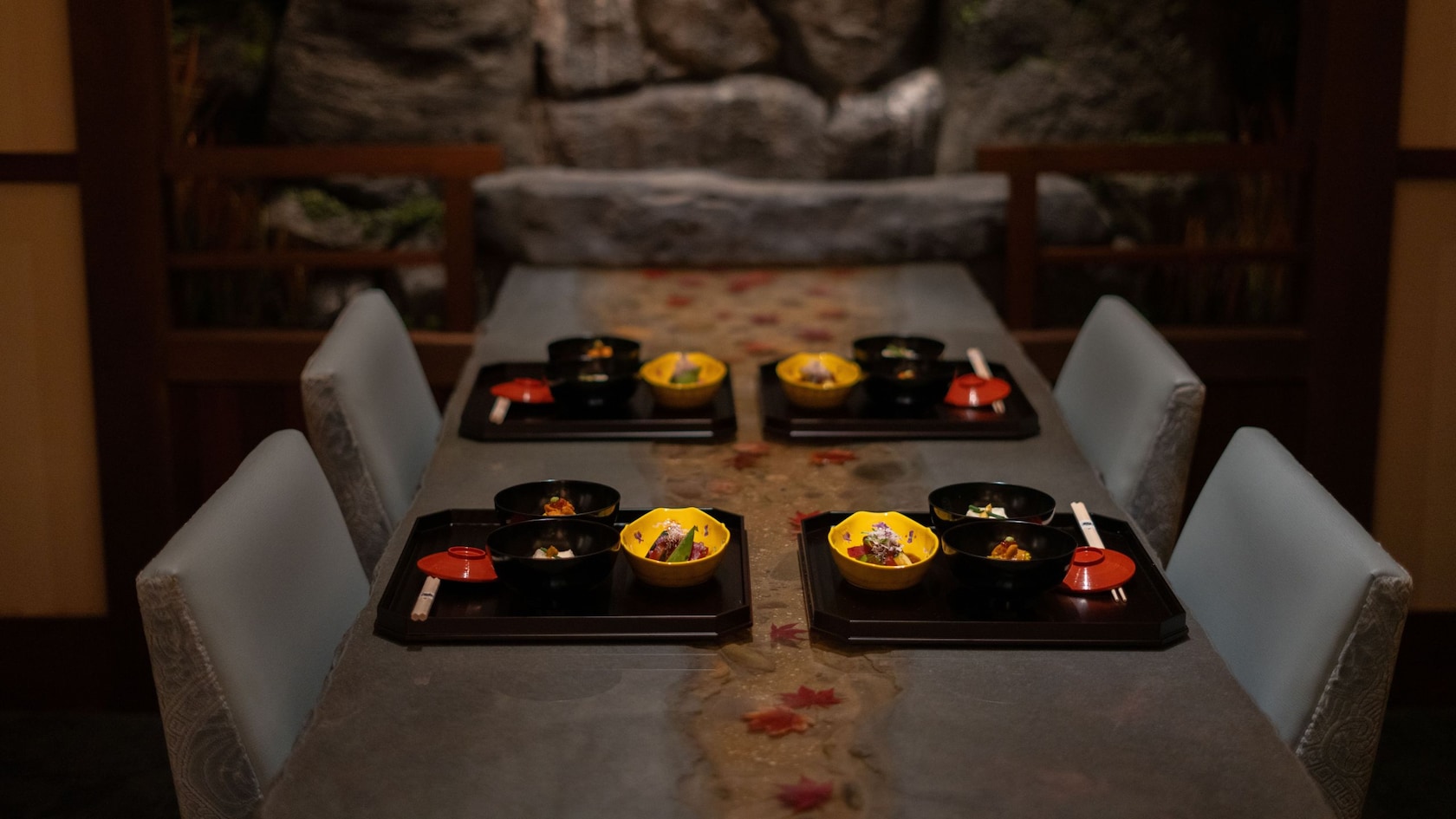 A dimly lit dinner table at Takumi-Tei set with 4 trays of food