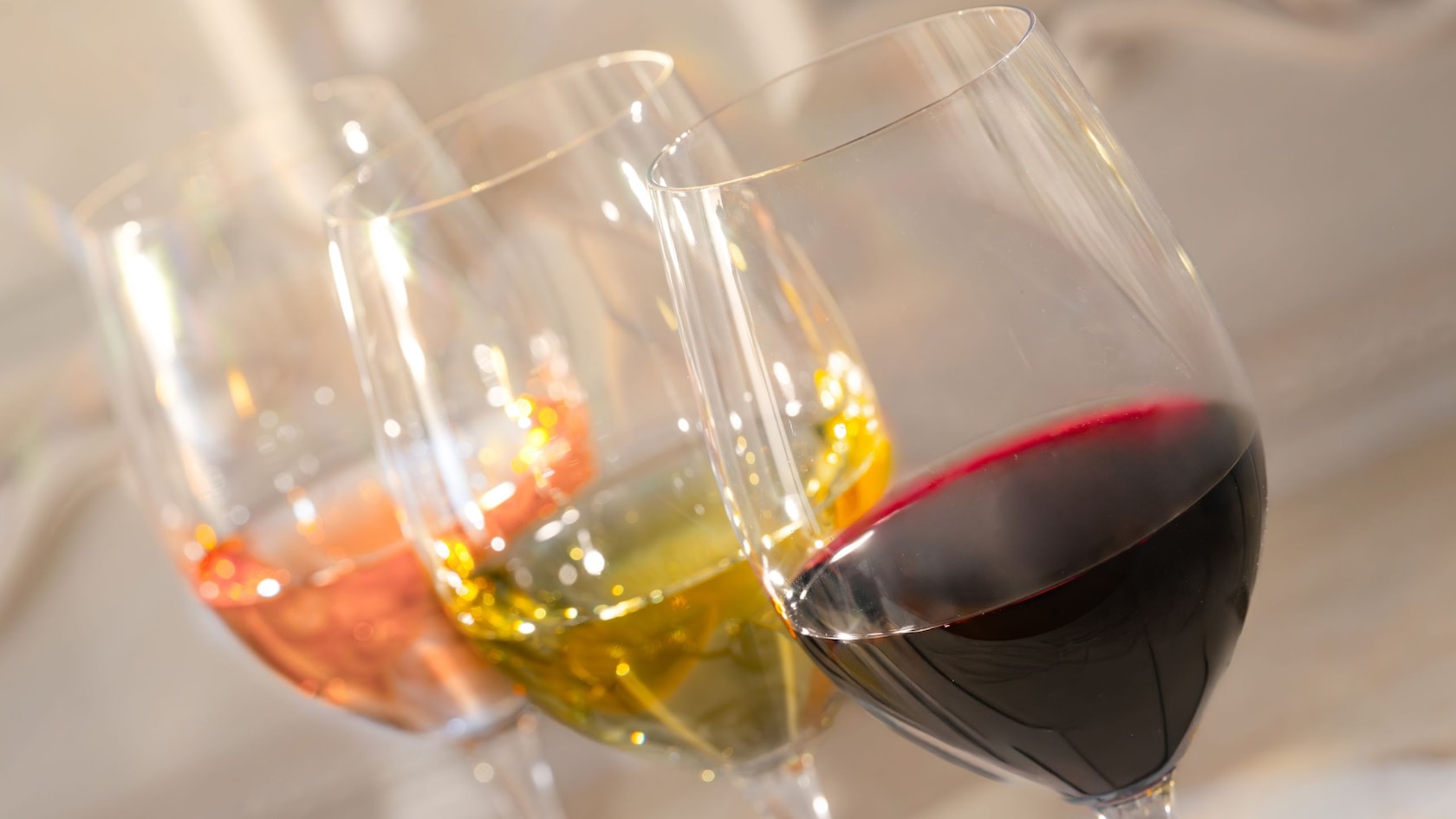 Una fila de tres copas de vino rellenas de vino rosado, blanco y tinto