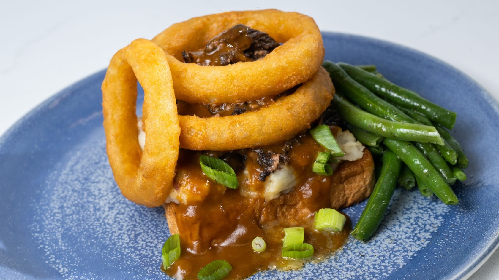 A pot roast covered with gravy and onion rings and a side of green beans