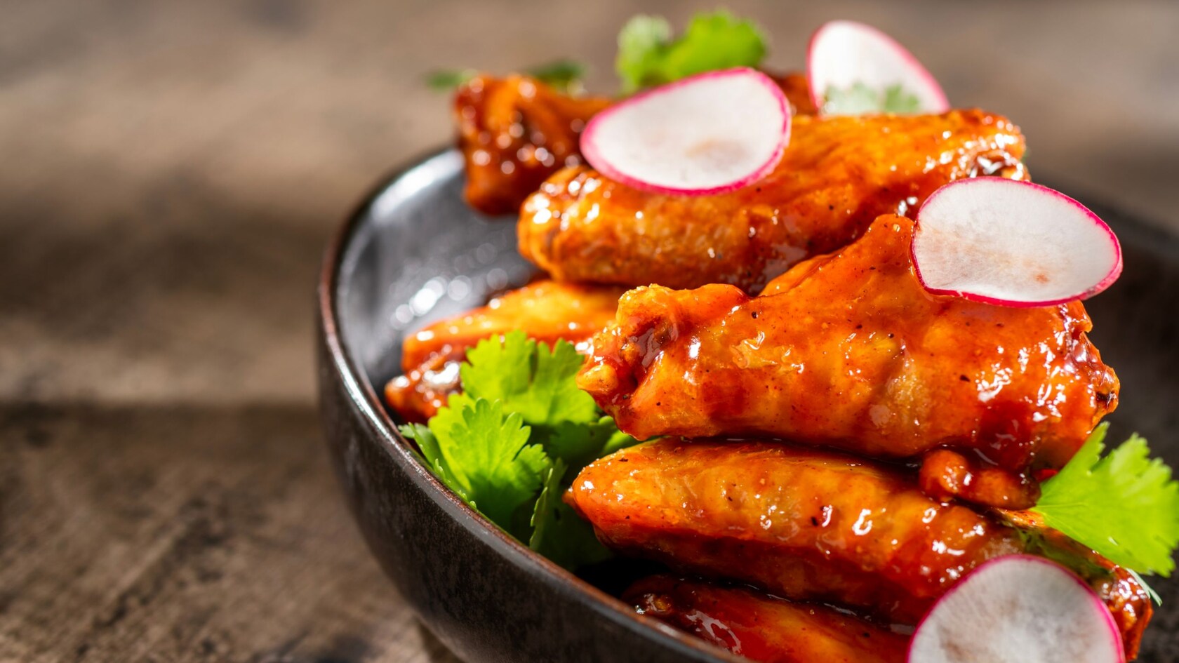 Alitas de pollo glaseadas decoradas con rodajas de rábano y cilantro en un tazón