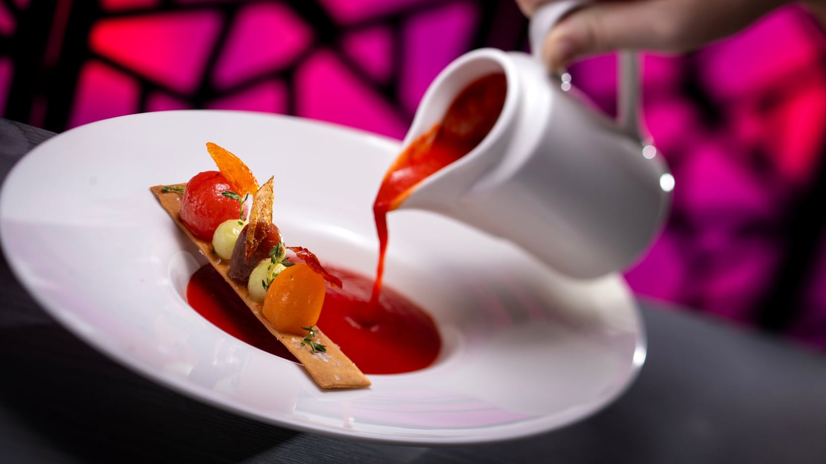 Uma pessoa servindo gazpacho da estação em uma tigela ao lado de um biscoito coberto com tomates do Toledo Tapas, Steak & Seafood