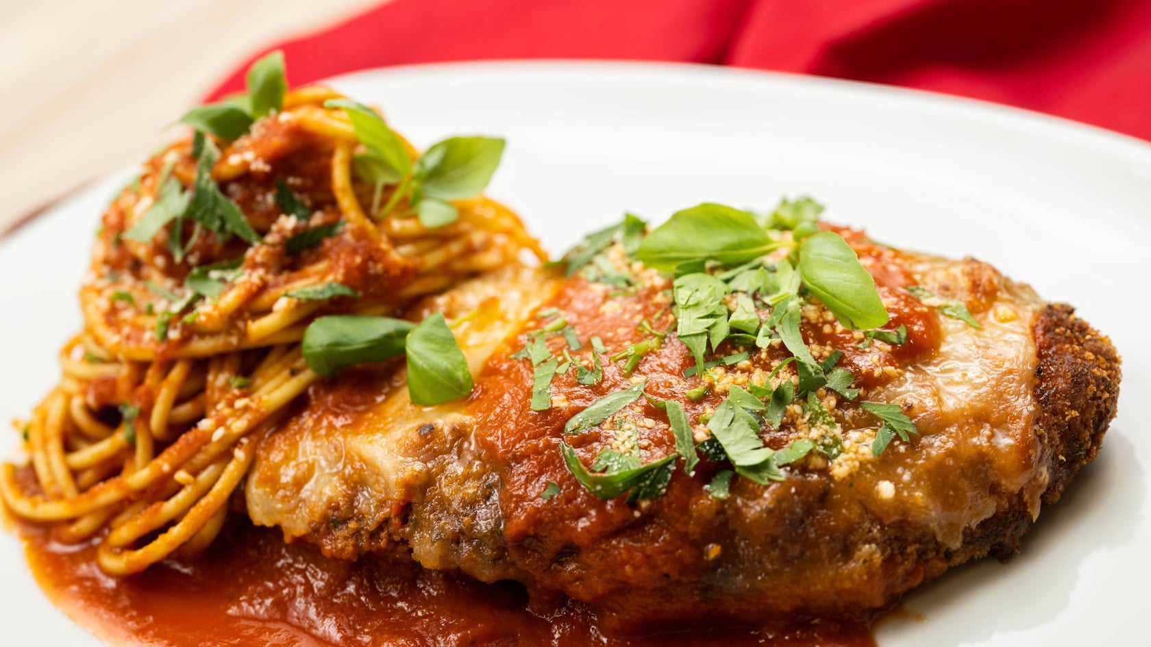 Breaded chicken parmigiana with a serving of spaghetti on a dish.