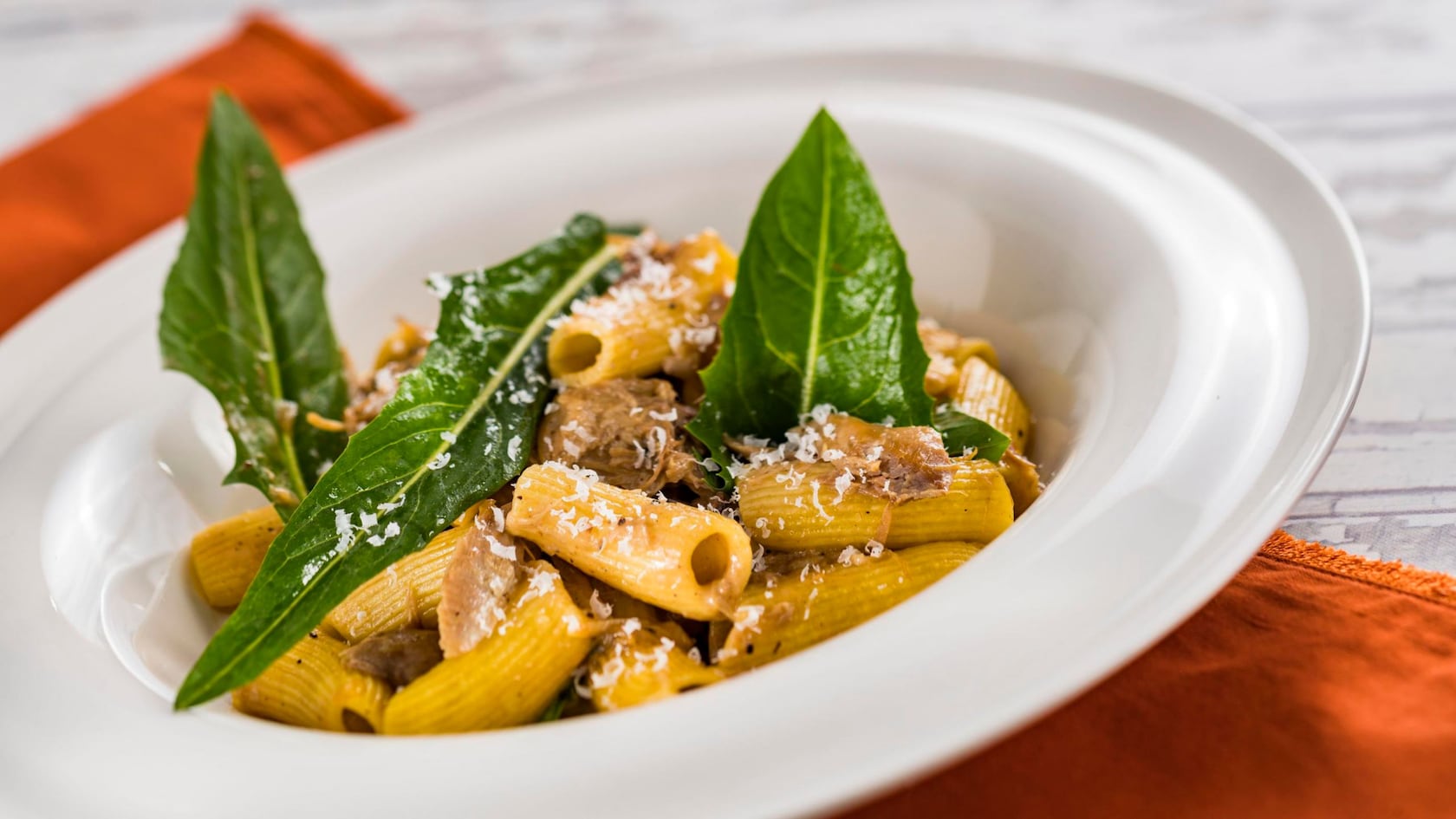 Un tazón de rigatoni adornado con hierbas frescas y queso