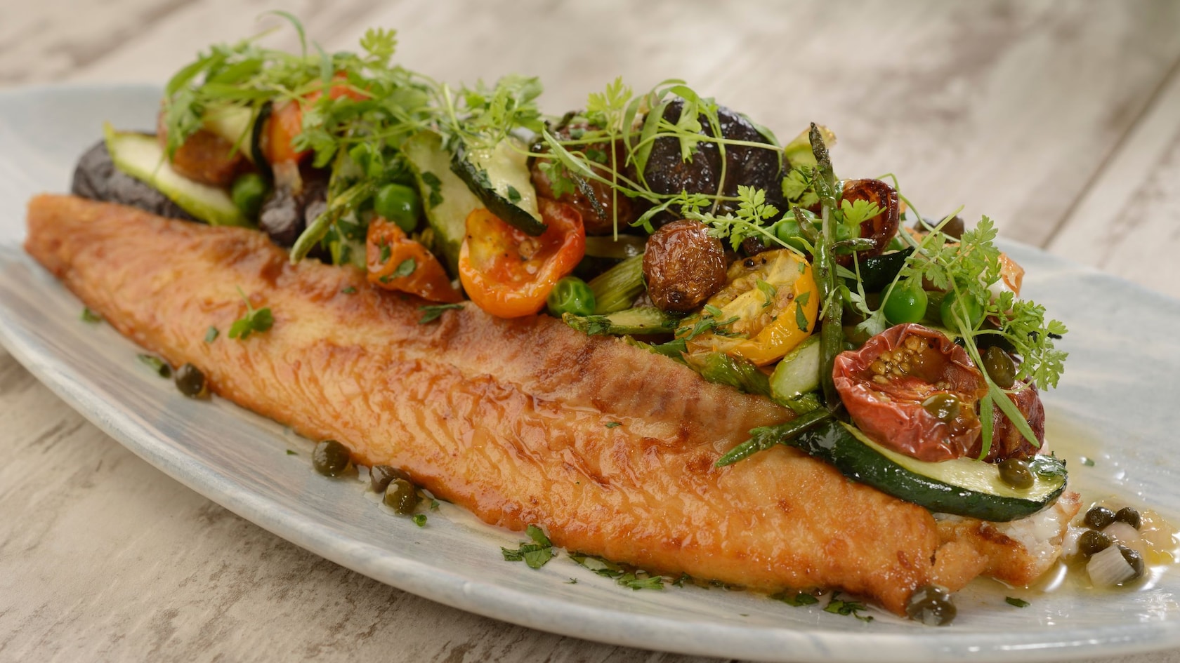 Un plato con un filete de pescado y una variedad de vegetales al costado