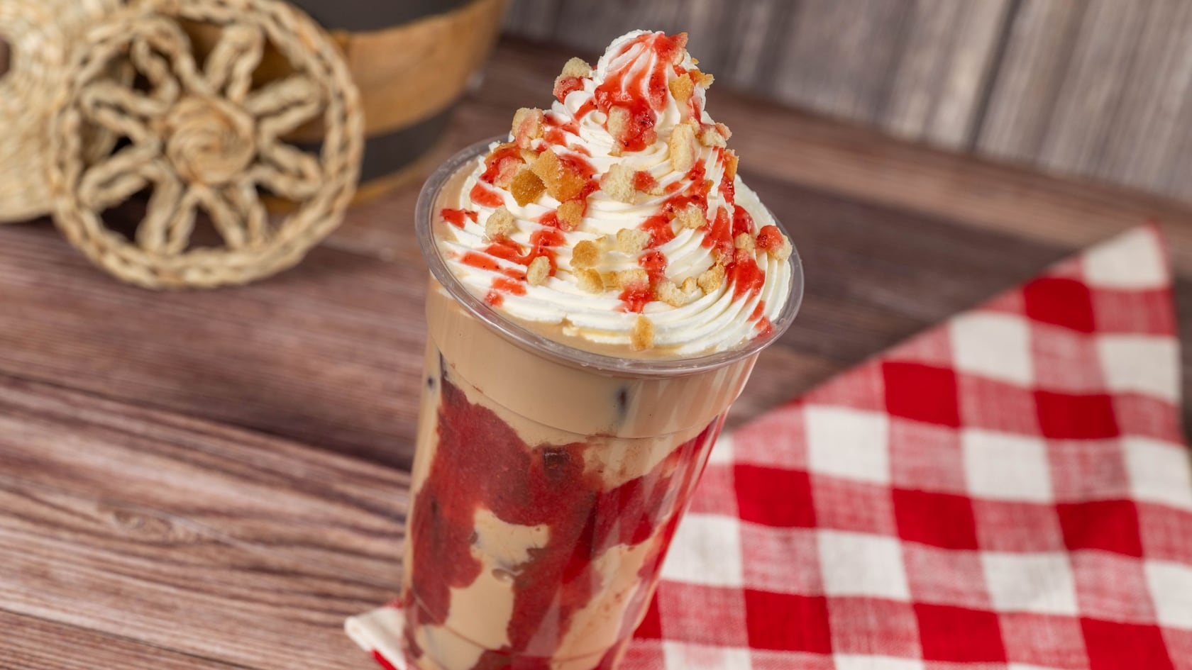 An iced latte layered with strawberry sauce and topped with whipped cream, strawberry drizzle and shortbread crumbles