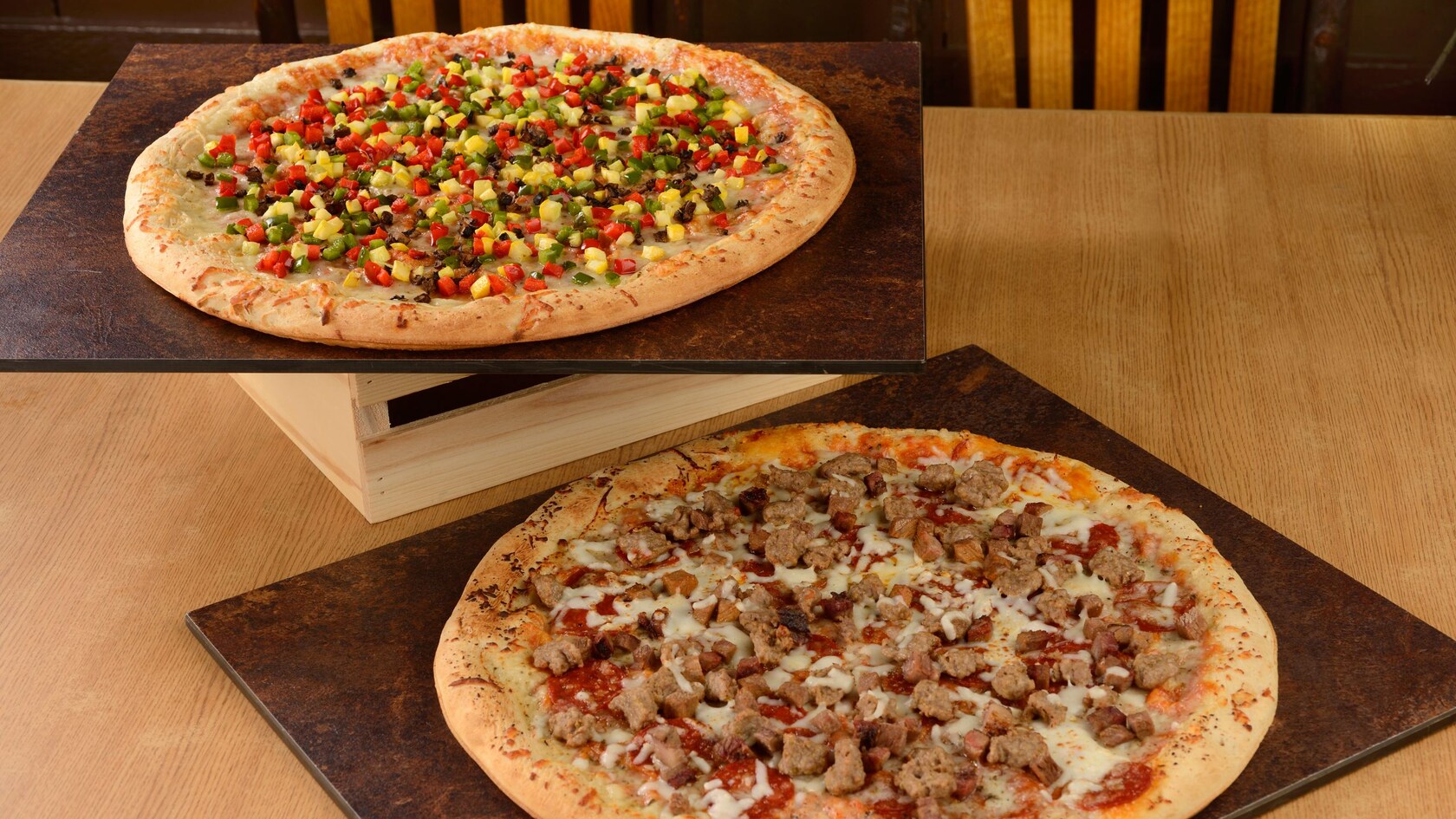 Two pizzas, with various vegetable and meat toppings, on serving platters