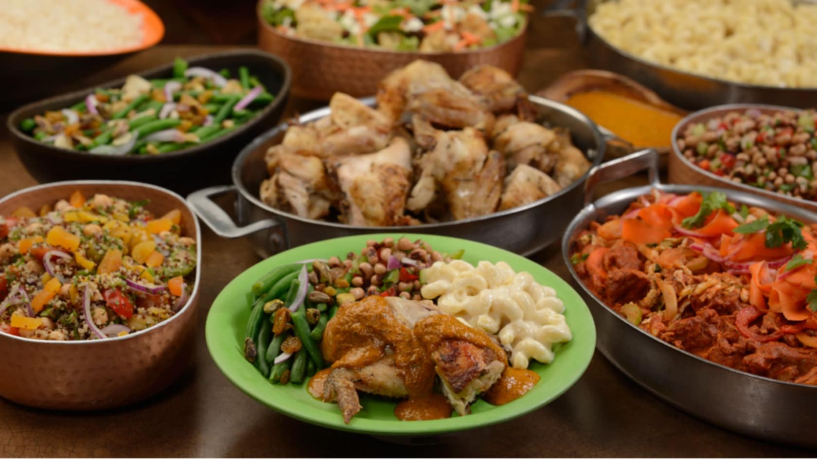 Several platters of lunch and dinner foods, including chicken, beef, green beans and assorted salads