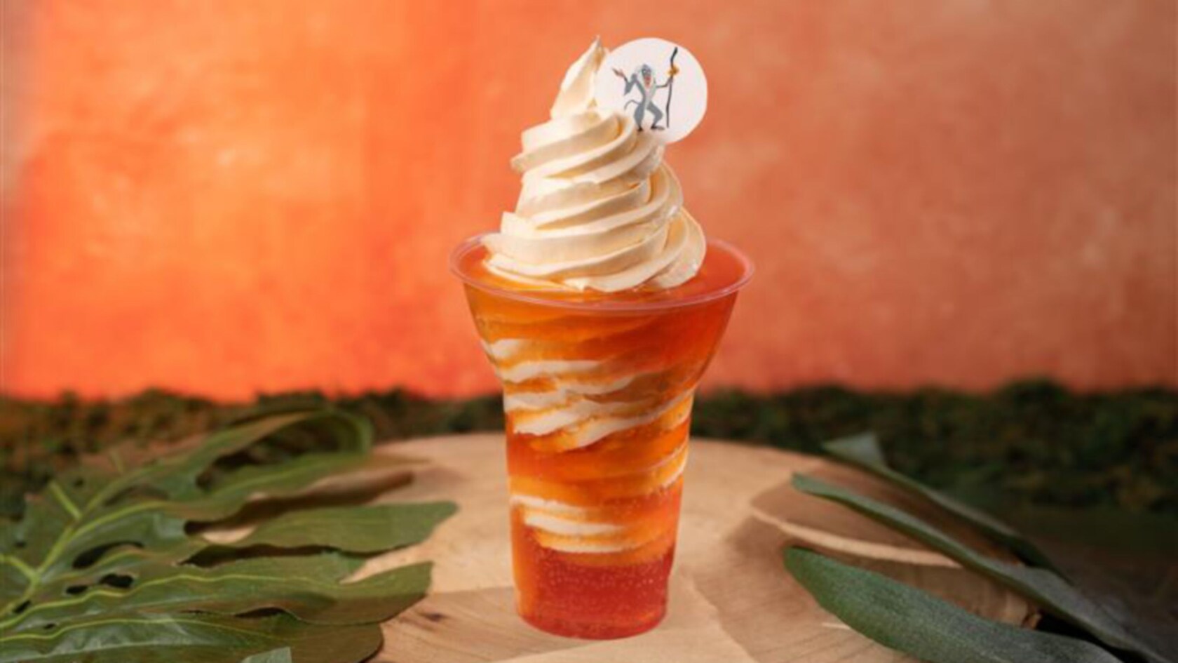 Soft serve ice cream swirled with orange soda in a cup with decorative topper featuring Rafiki