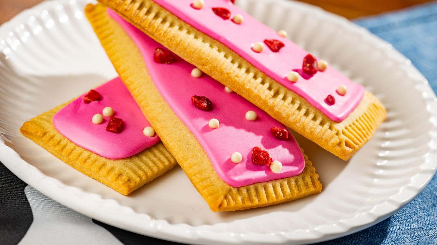 Pastries topped in frosting, bacon and candy resting on a plate and a tablecloth