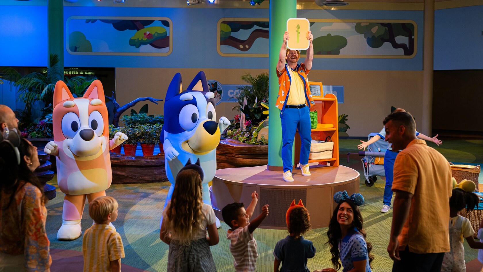 Bluey and Bingo characters on stage with a performer holding an asparagus sign